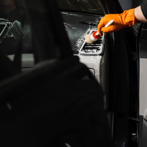 Cleaning with air and brush of air conditioning system in the car. Worker in detailing auto service clean elements of interior of car