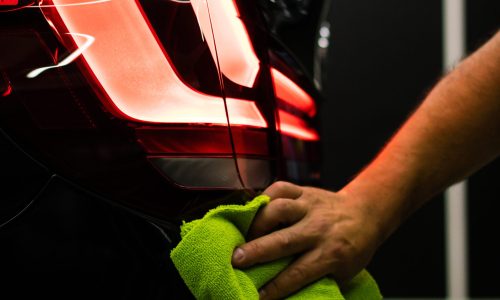 A selective focus shot of a man cleaning car's back headlight with a microfiber cloth